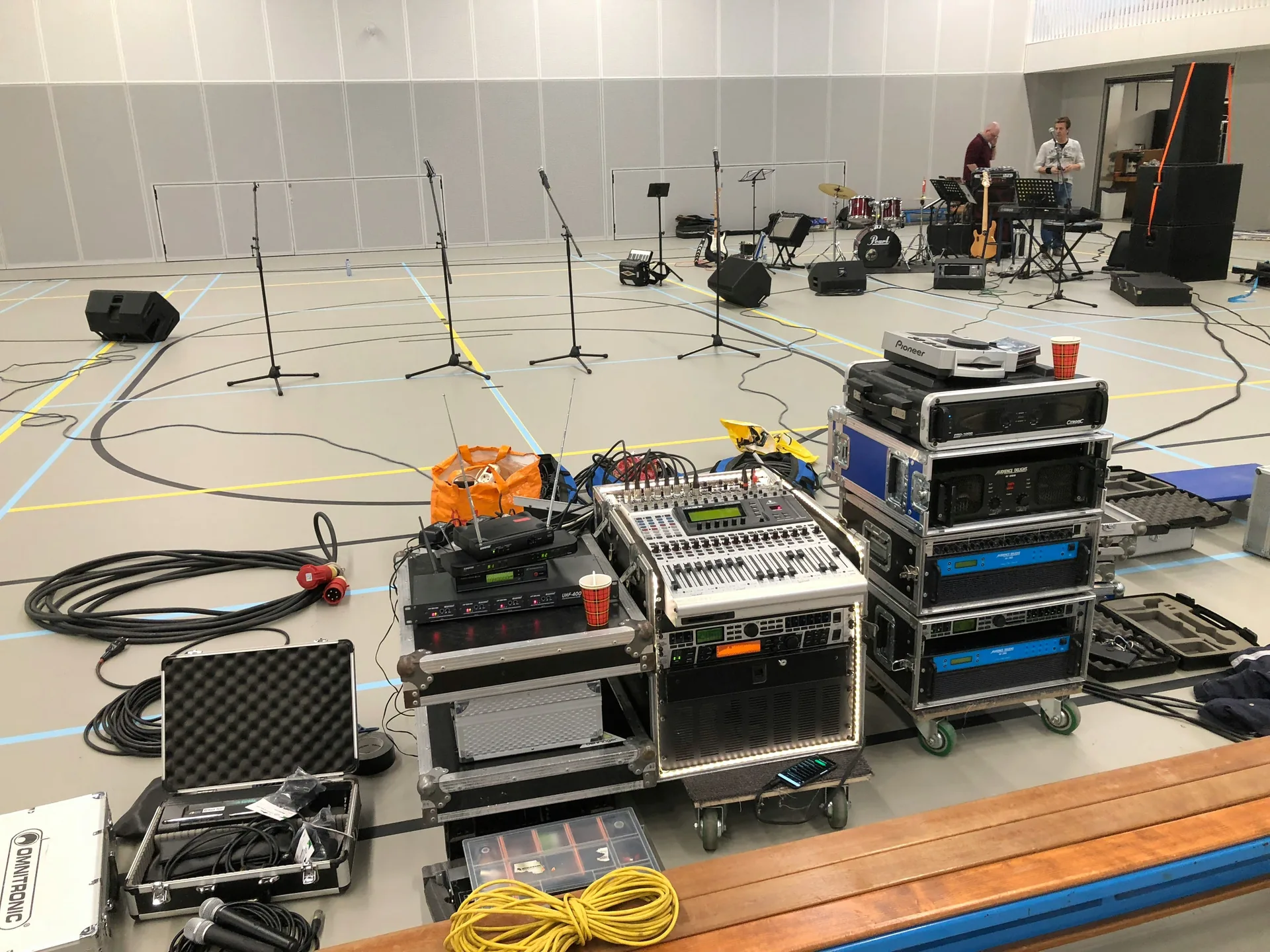 AV technician setting up sound equipment in gymnasium before soundcheck with microphones and cases