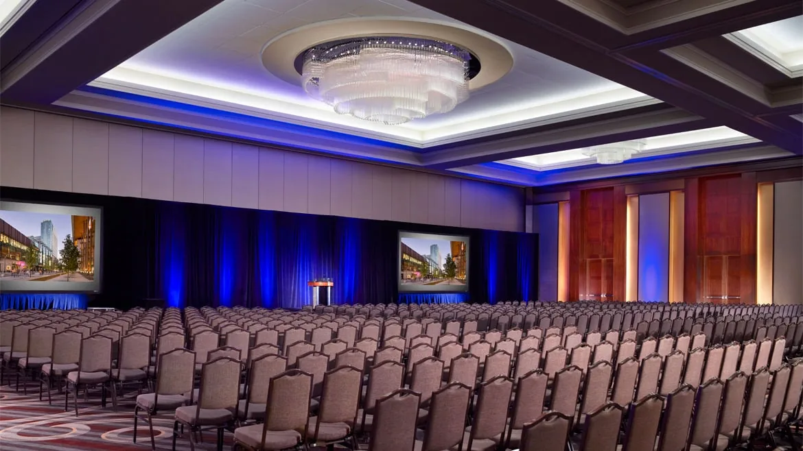 Modern conference hall with rows of chairs, projection screen stage and elegant lighting