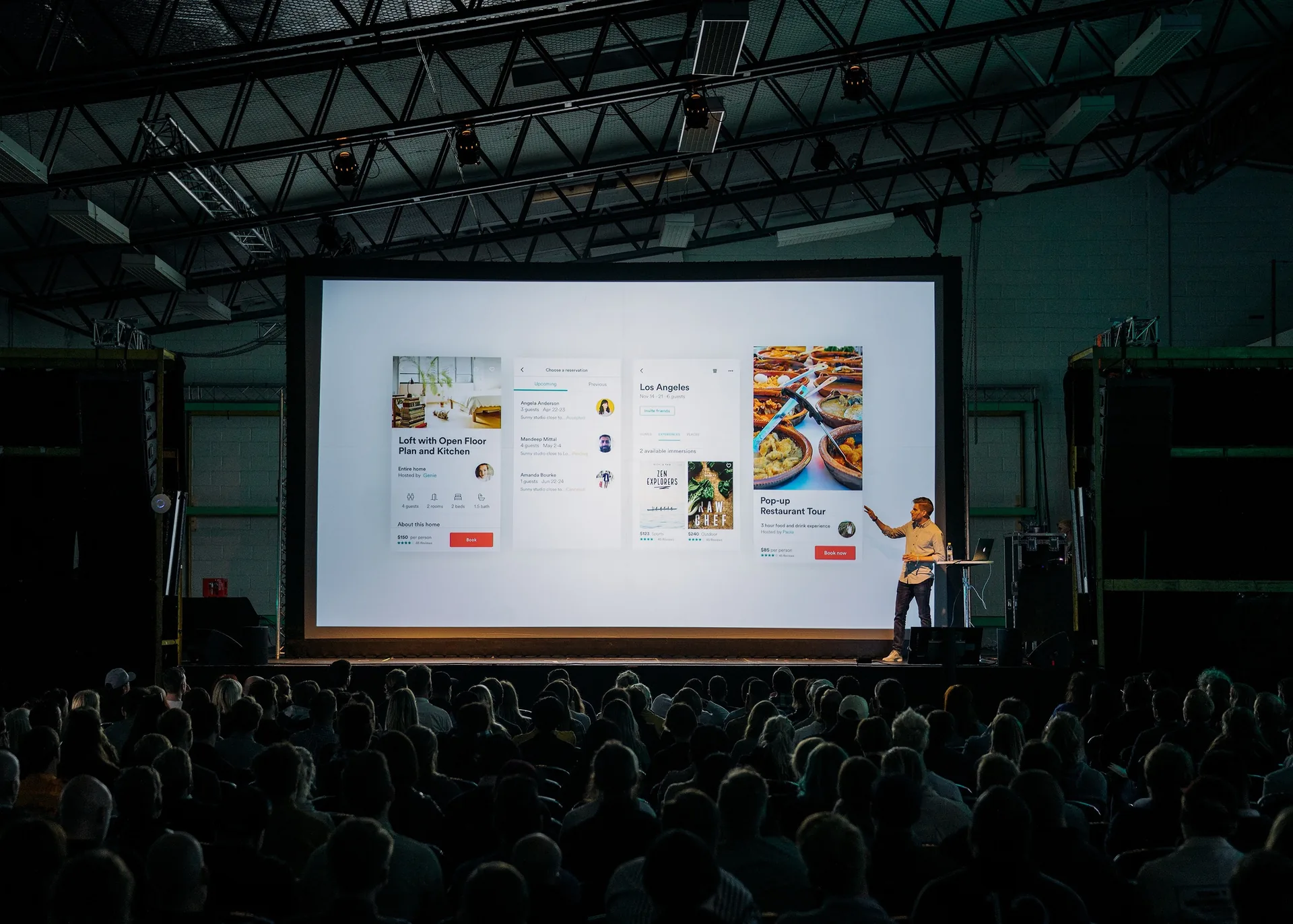 Presenter on stage at a corporate conference with large display screen and seated audience