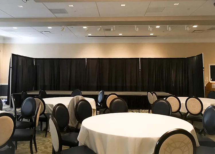 Corporate conference with black pipe and drape backdrop behind a presentation stage