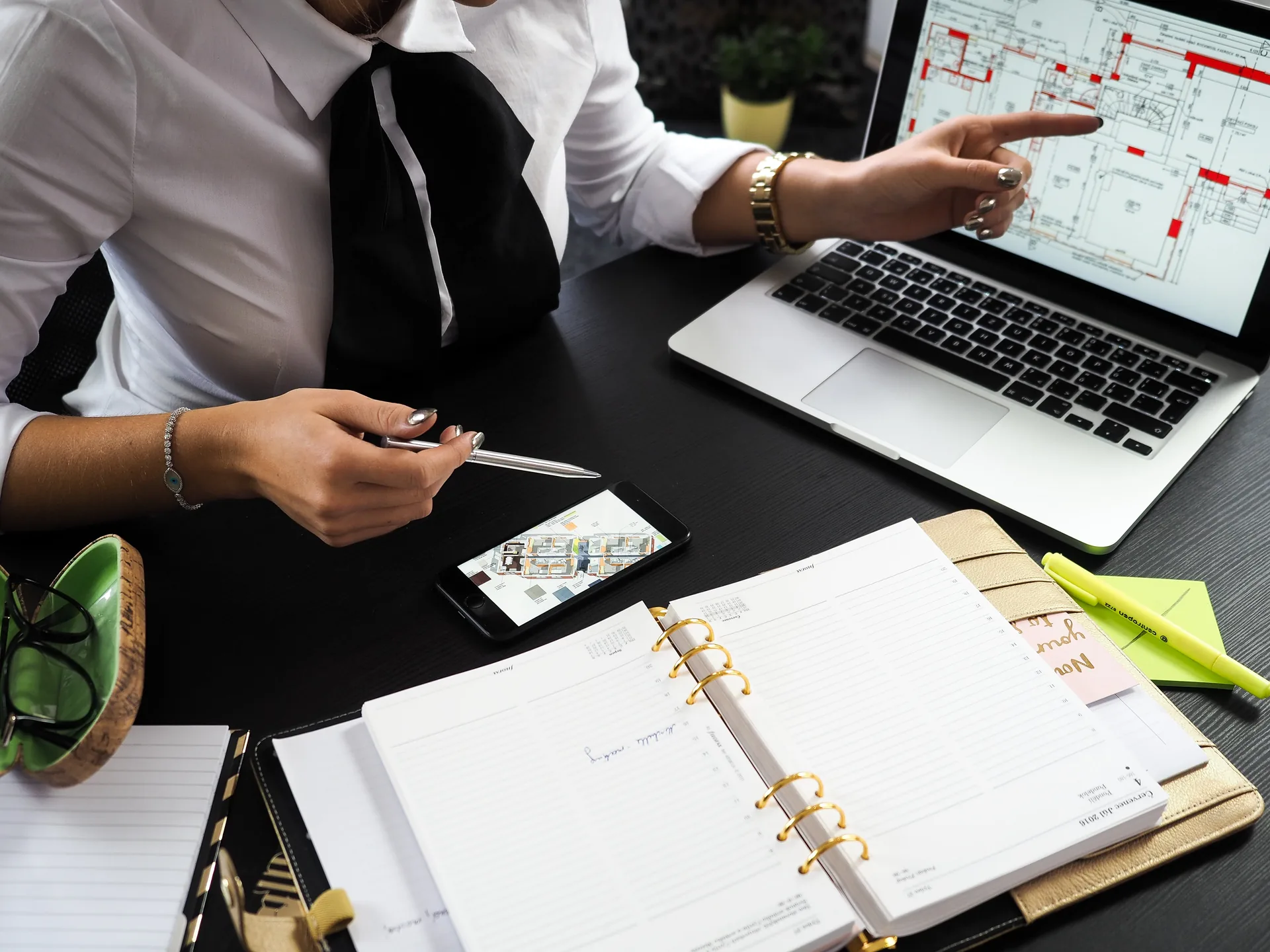 Event planner pointing at laptop showing floor plans with notebook and planning materials