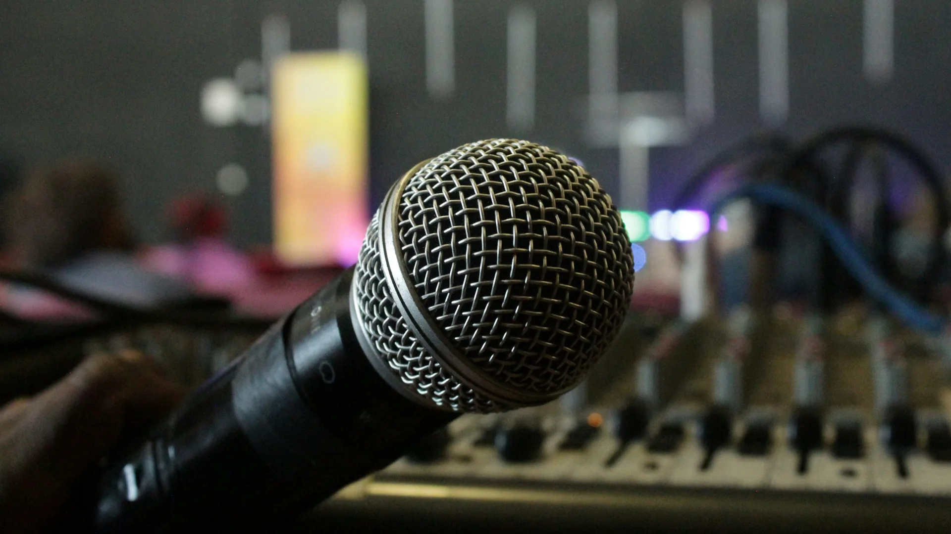 Handheld microphone positioned in front of an audio mixing console with faders