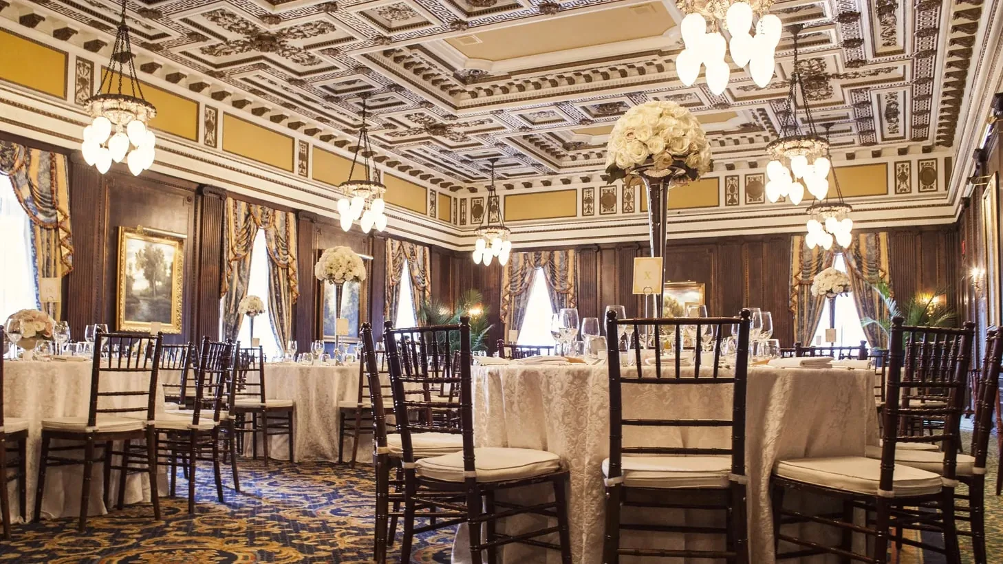 Grand ballroom with chandeliers, draped windows and banquet tables set for formal event