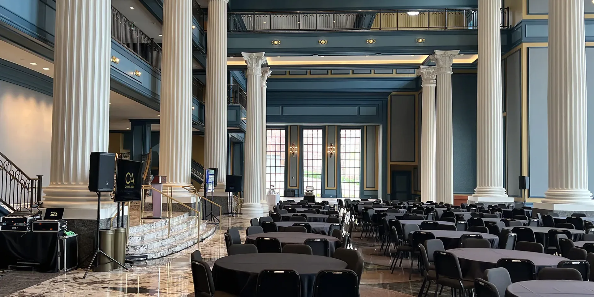 Large hotel ballroom set for a corporate event with speakers, presentation displays and banquet seating.