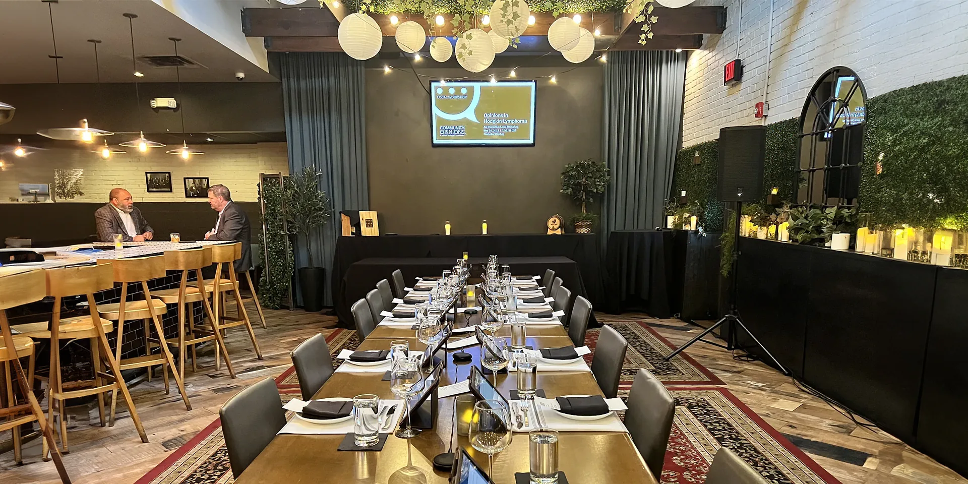 Corporate hotel event setup with a presentation display and powered speaker beside a seated dining area.