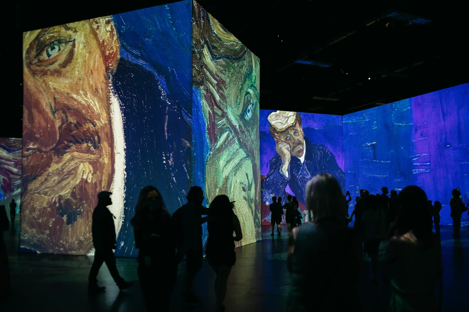 Art gallery space with large colorful Van Gogh projections displayed on walls with visitors viewing