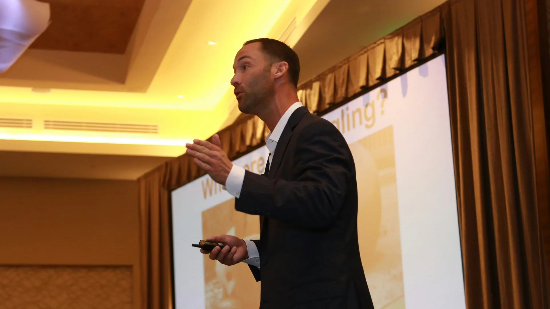 Keynote speaker presenting on stage with projection screen and event lighting for conference