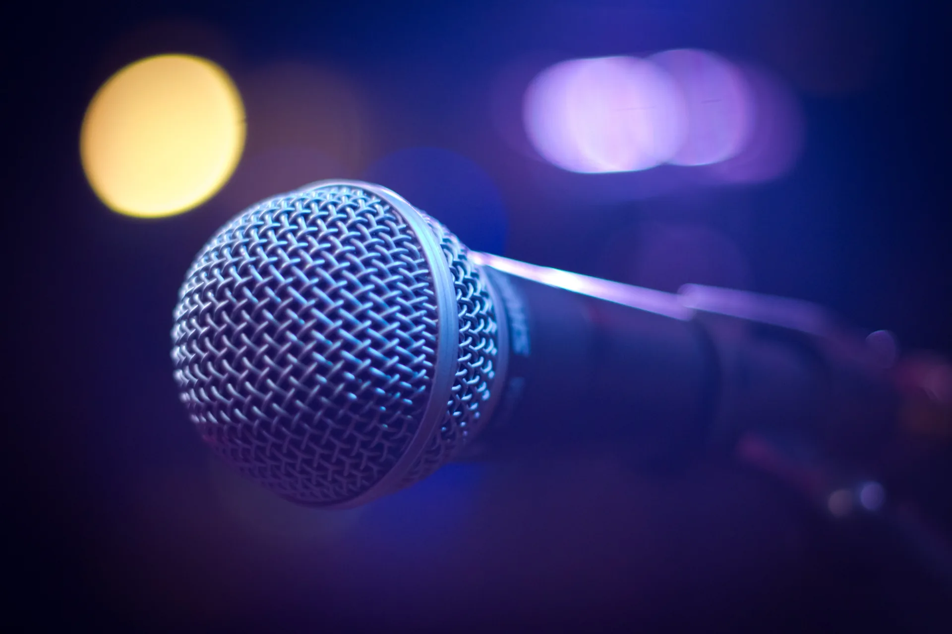 Close-up of a professional stage microphone with colorful bokeh concert lighting in the background
