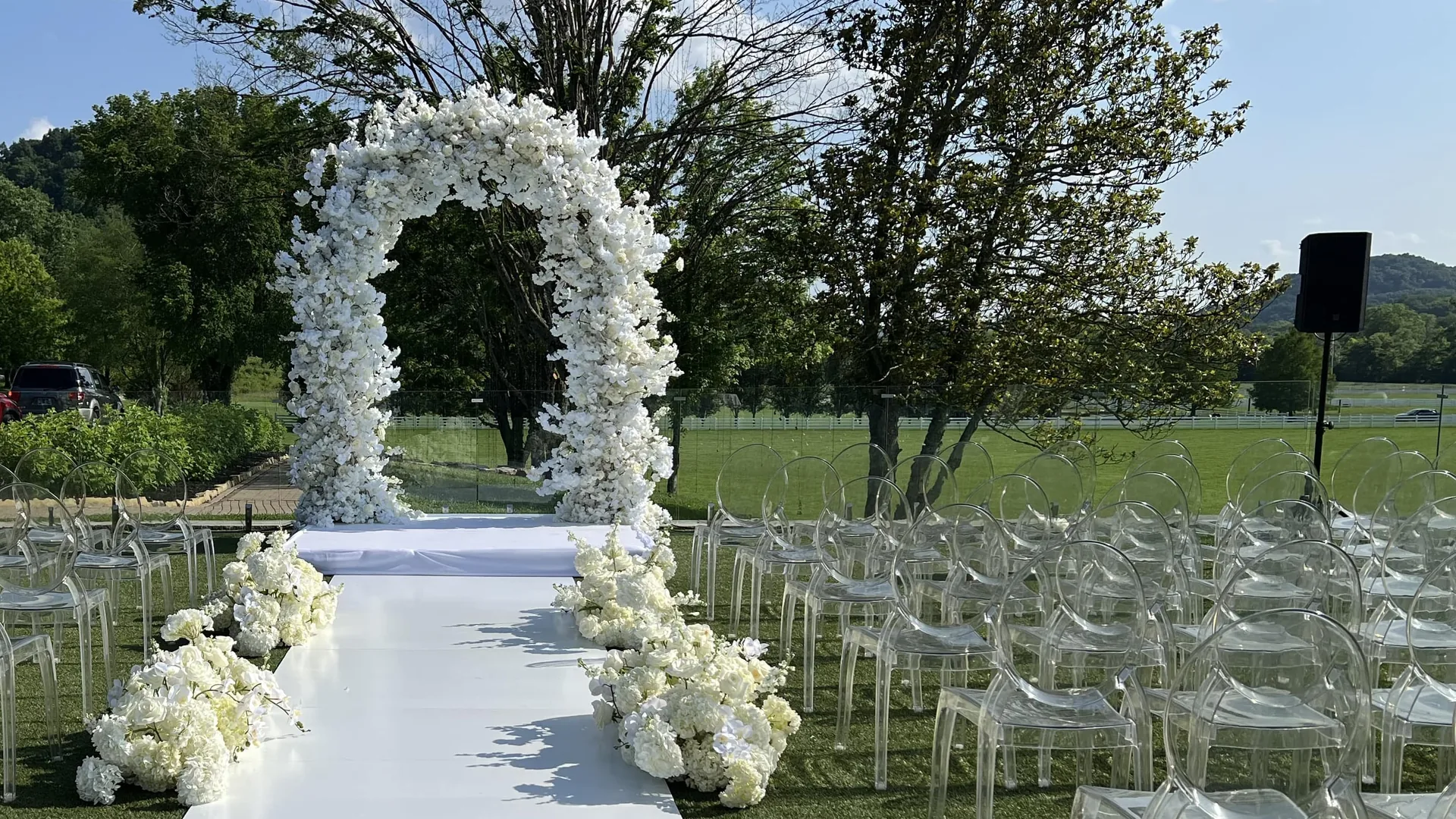 Outdoor wedding ceremony with portable PA speaker on stand and transparent acrylic chairs