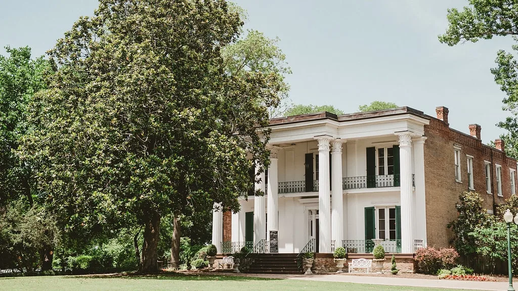 Riverwood Mansion exterior showing white columns, grand entrance steps and surrounding greenery