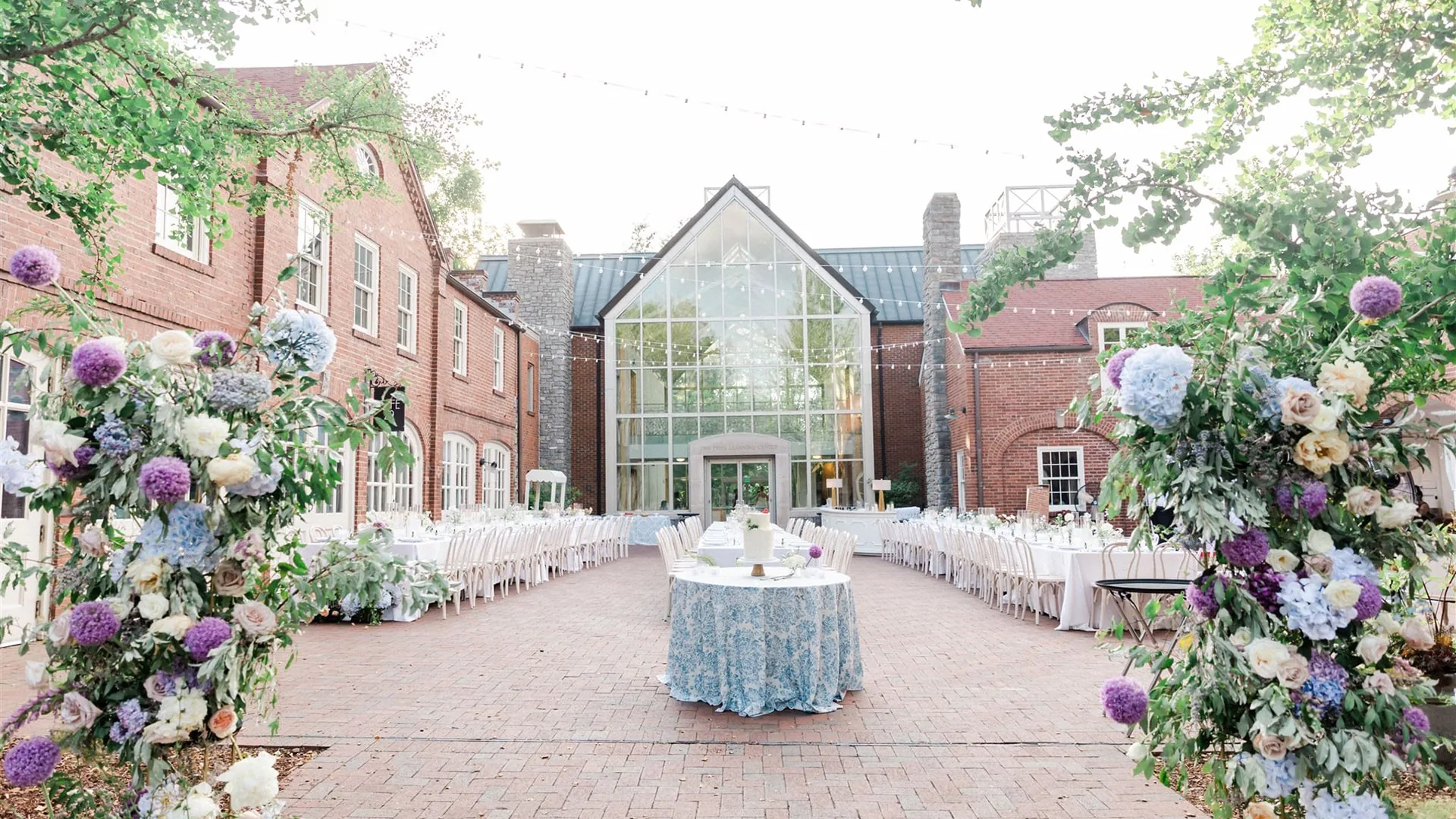 Outdoor wedding reception with white chairs, floral arrangements and string lights at Cheekwood