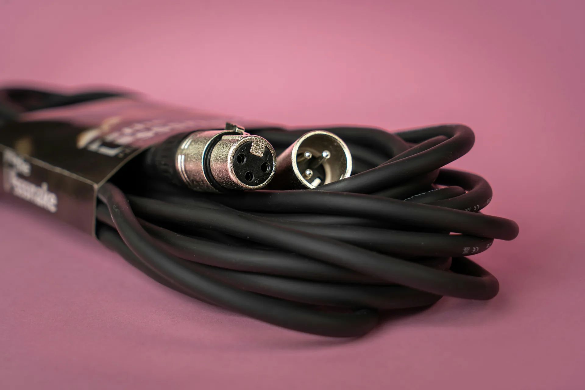 Coiled XLR audio cable with male and female connectors on pink background