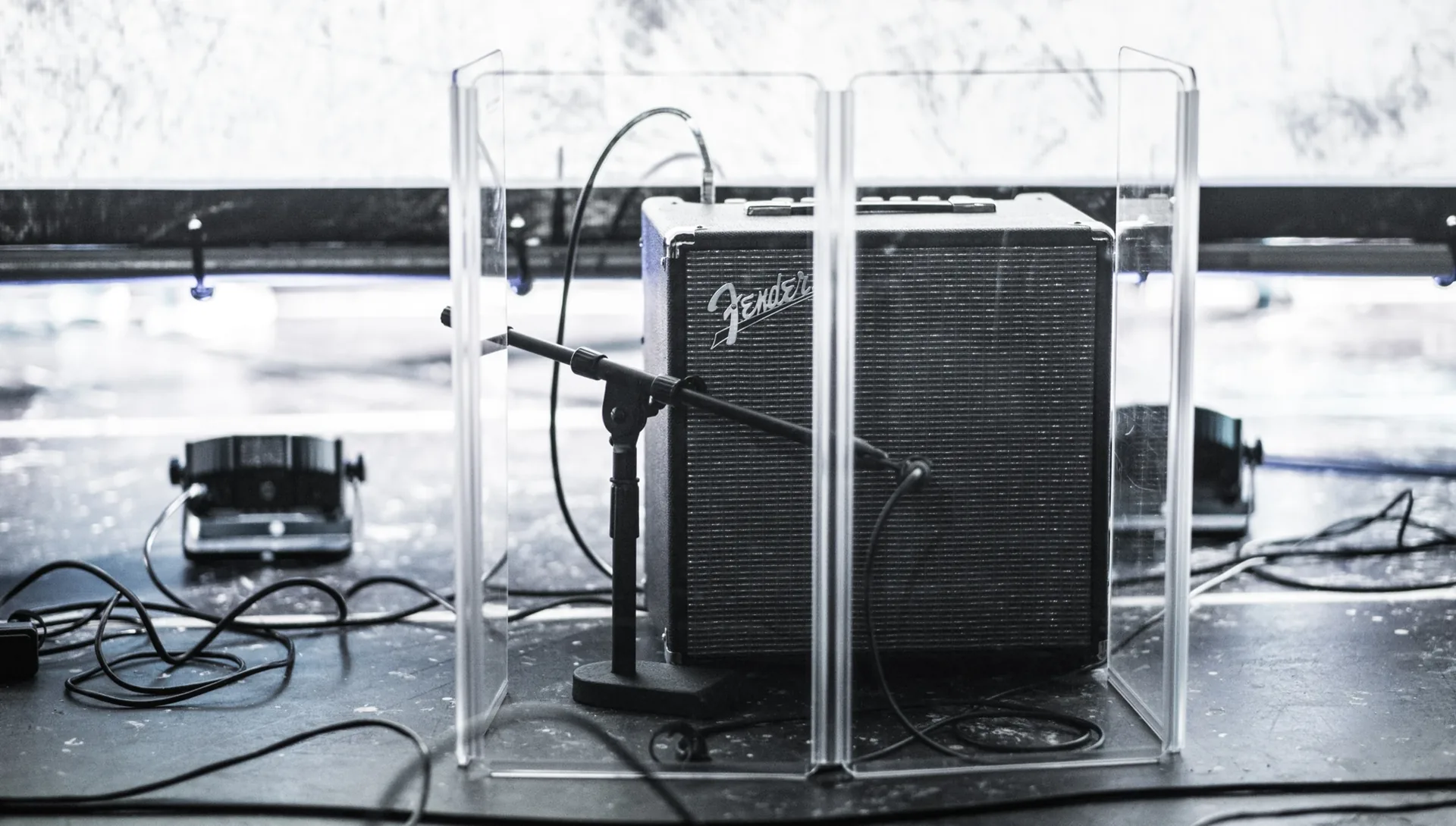 Shure SM57 microphone positioned close in front of a Fender guitar amplifier on stage with clear acrylic sound baffles