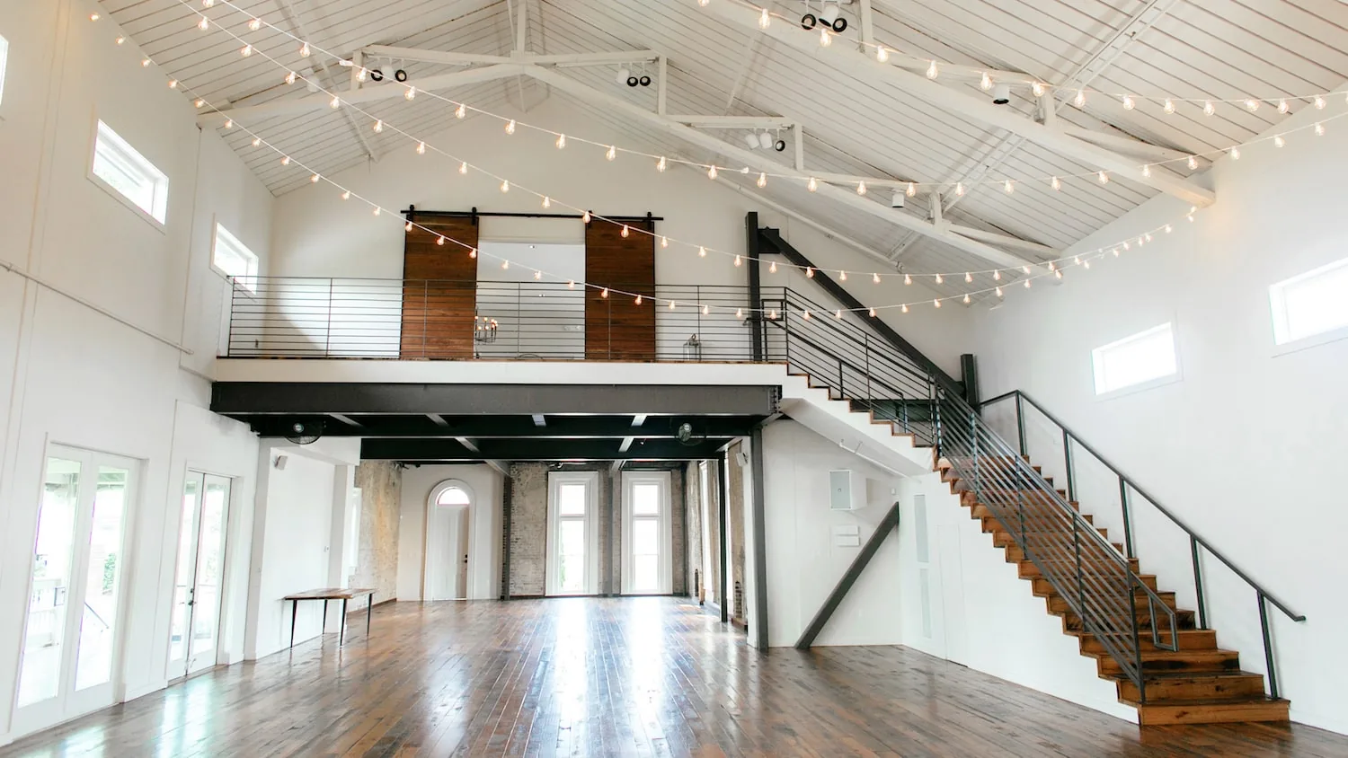 Loft-style event space with string lights, exposed brick, wooden floors and modern staircase