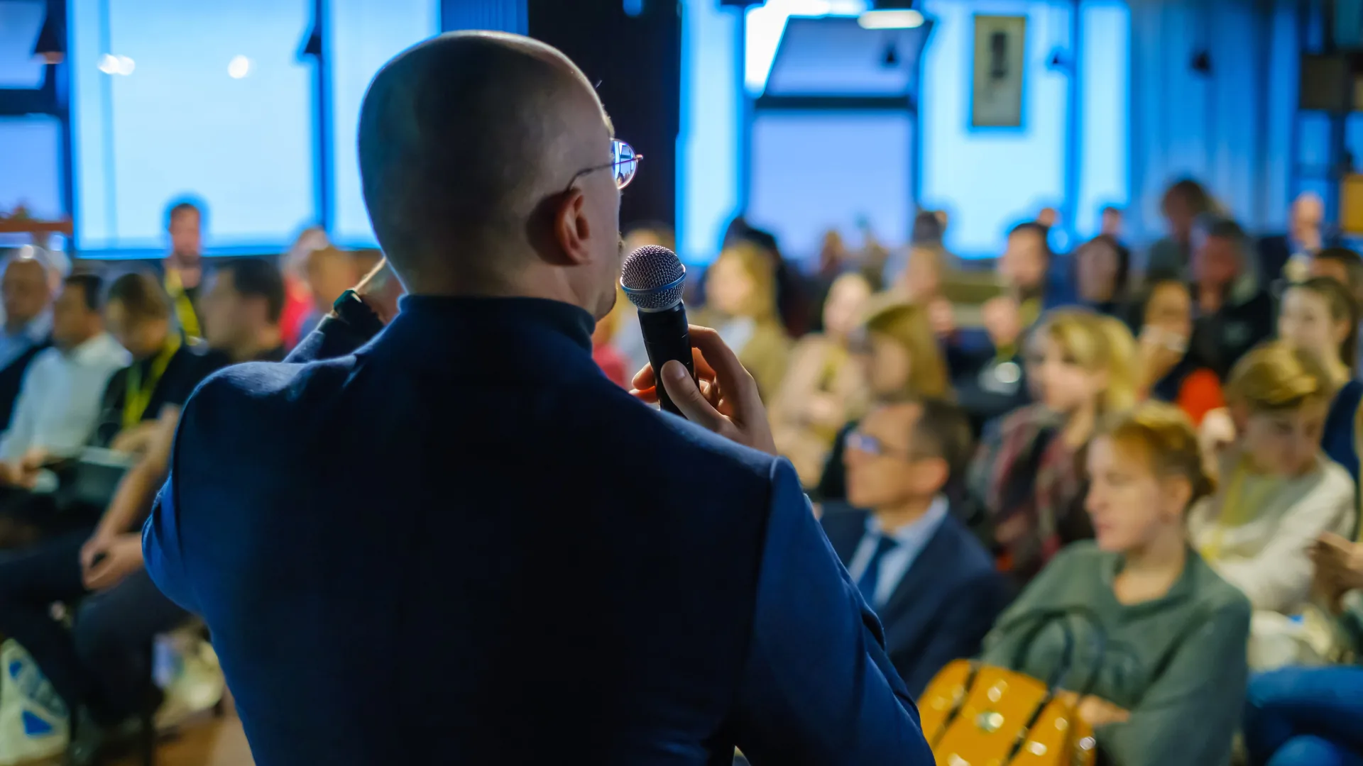 Professional speaker addressing corporate audience while using wireless microphone and AV support