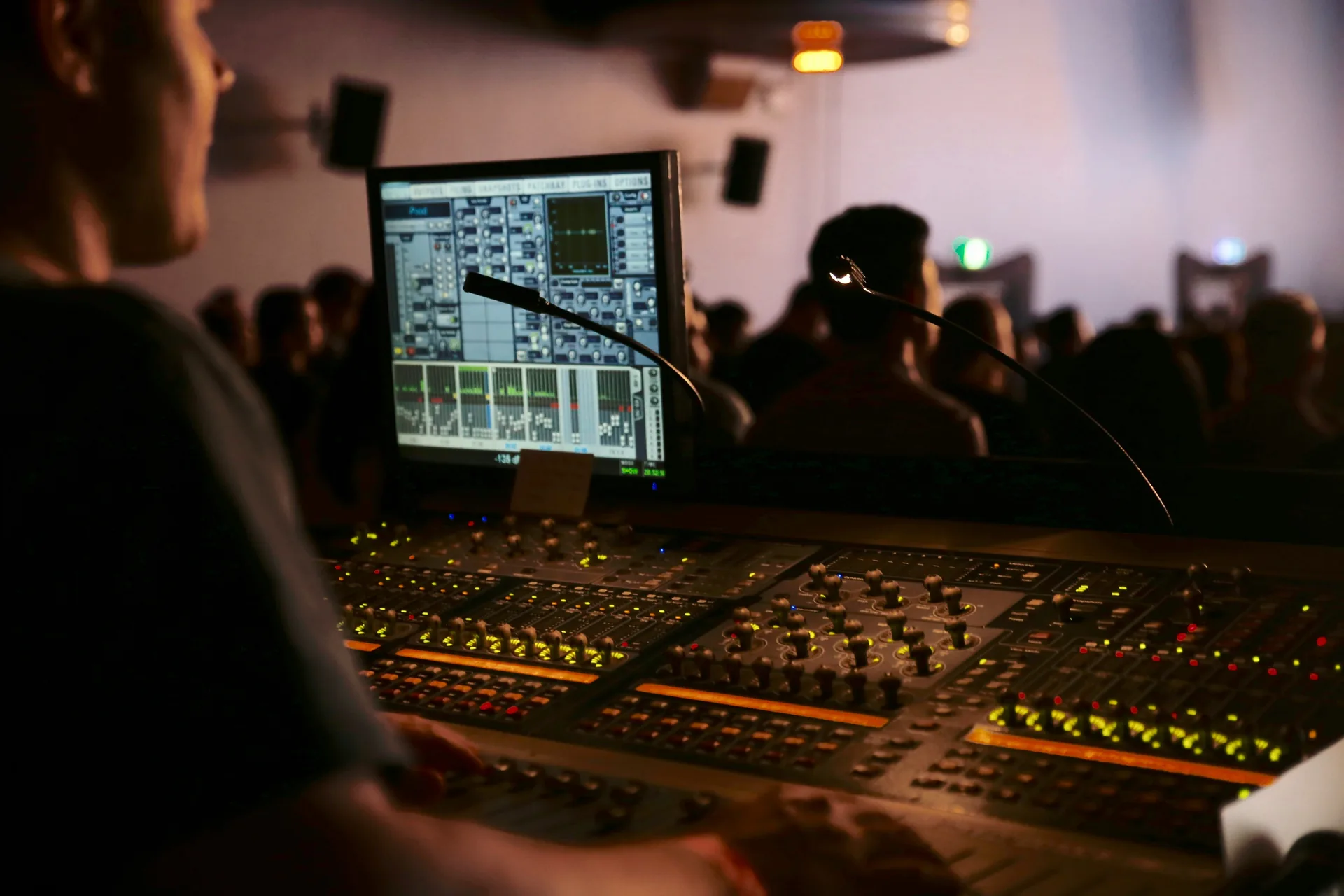 Technician troubleshooting audio at digital mixing console during live event with crowd in background