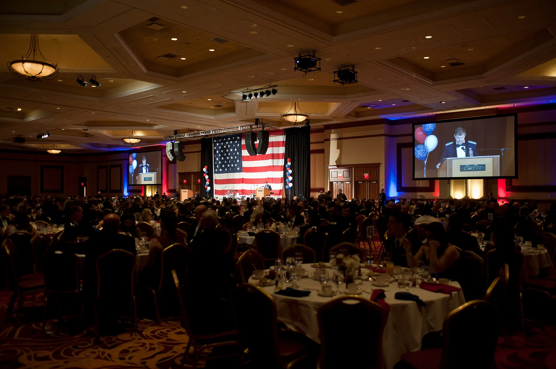 Conference presentation in a hotel banquet room with a presenter at a podium and projected screen