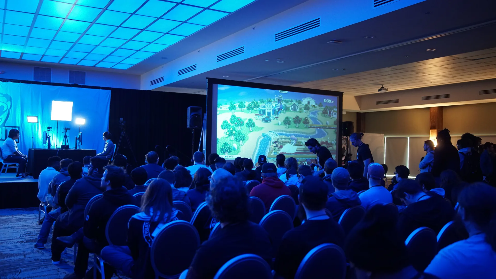 Esports tournament venue with large projector screen displaying game footage and audience seating