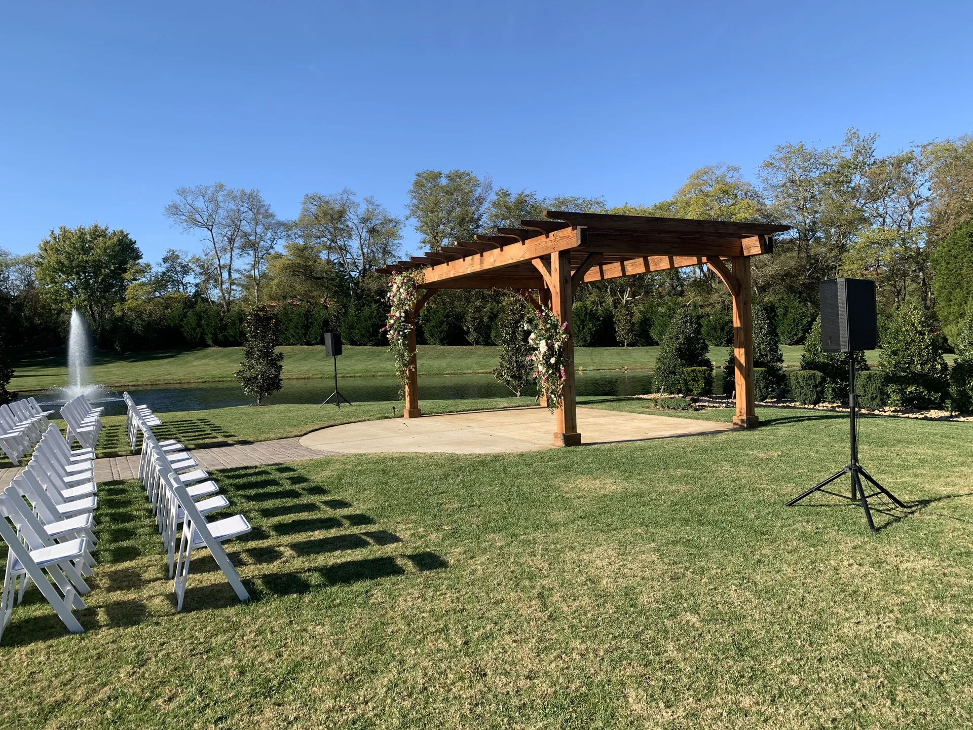 Outdoor wedding ceremony space with wooden pergola and fountain with empty chairs arranged