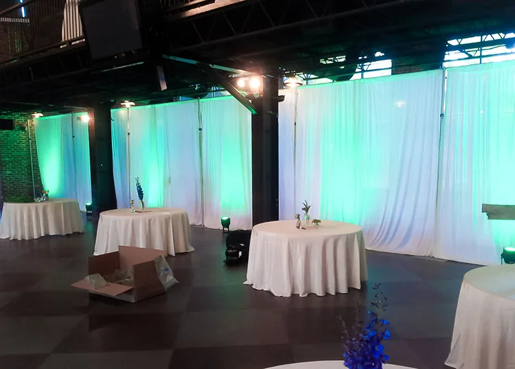 White drape backdrop with warm uplighting at a wedding reception venue