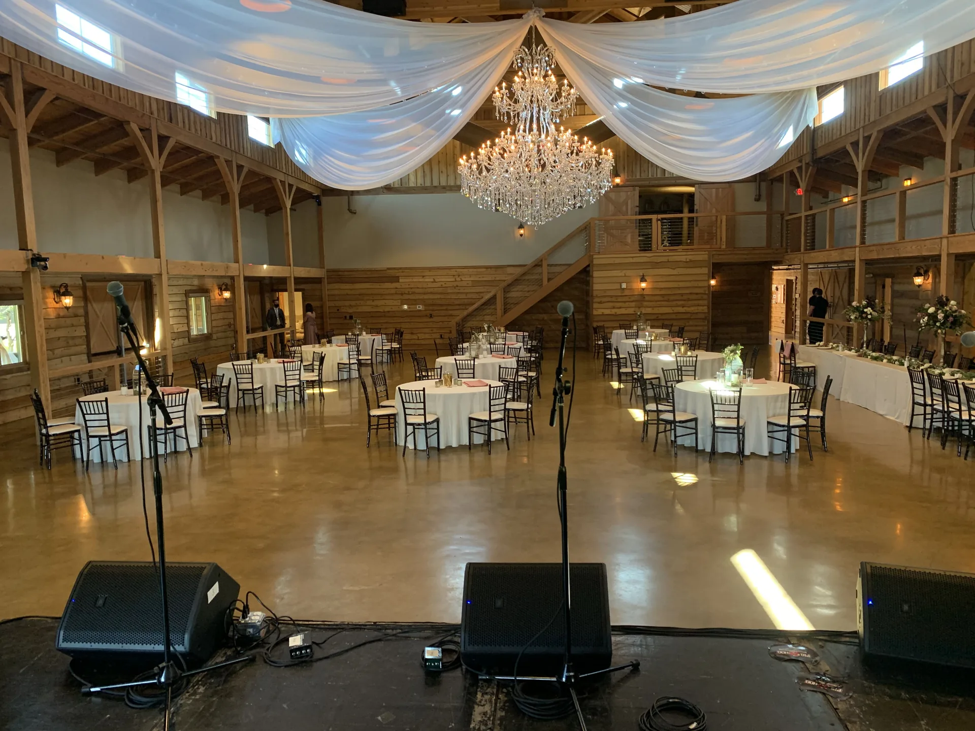 Barn wedding audio setup with PA speakers, floor monitors and microphone stands beneath white draping