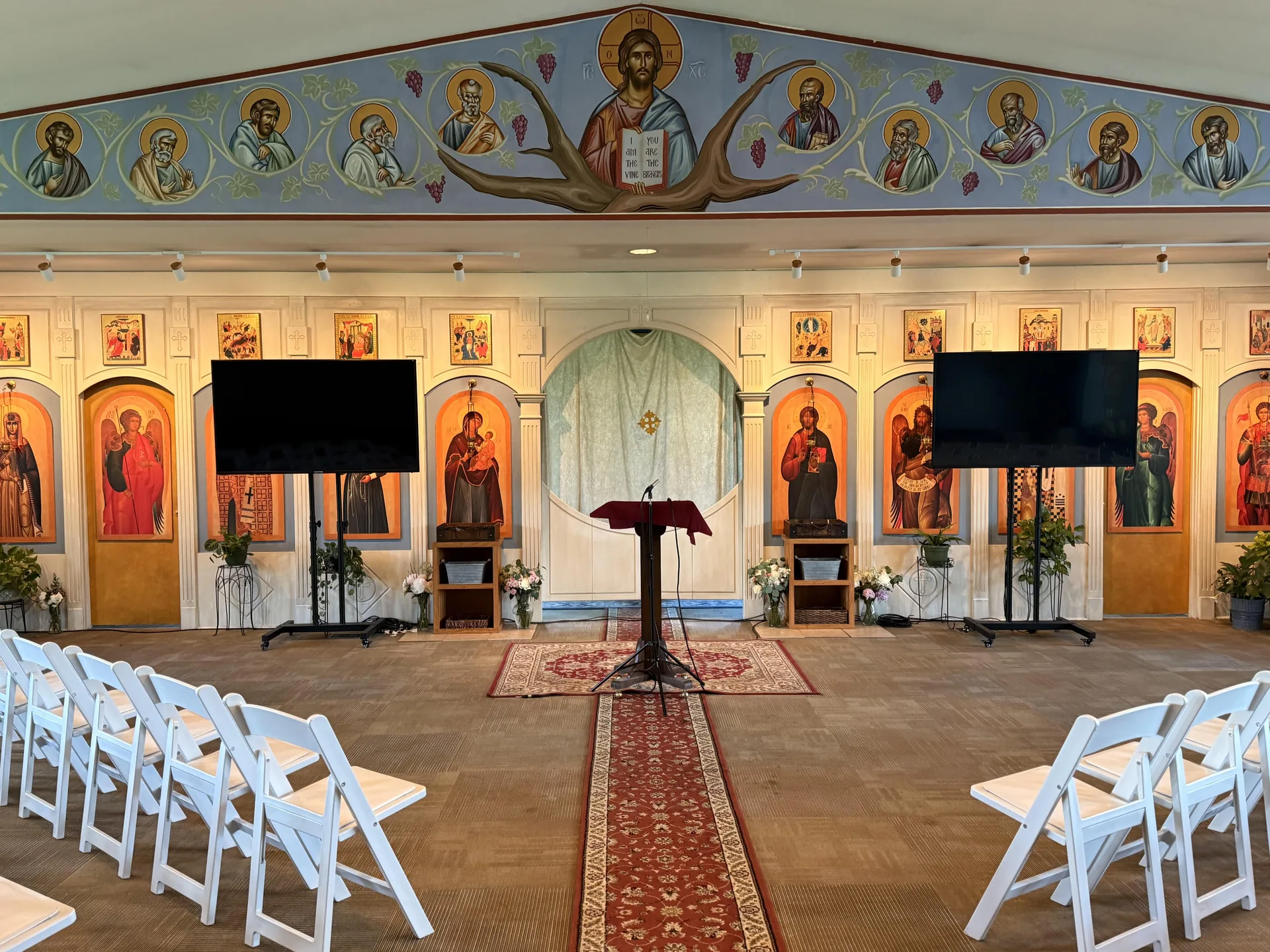 Church event setup with two TV displays on floor stands, a podium and rows of white chairs