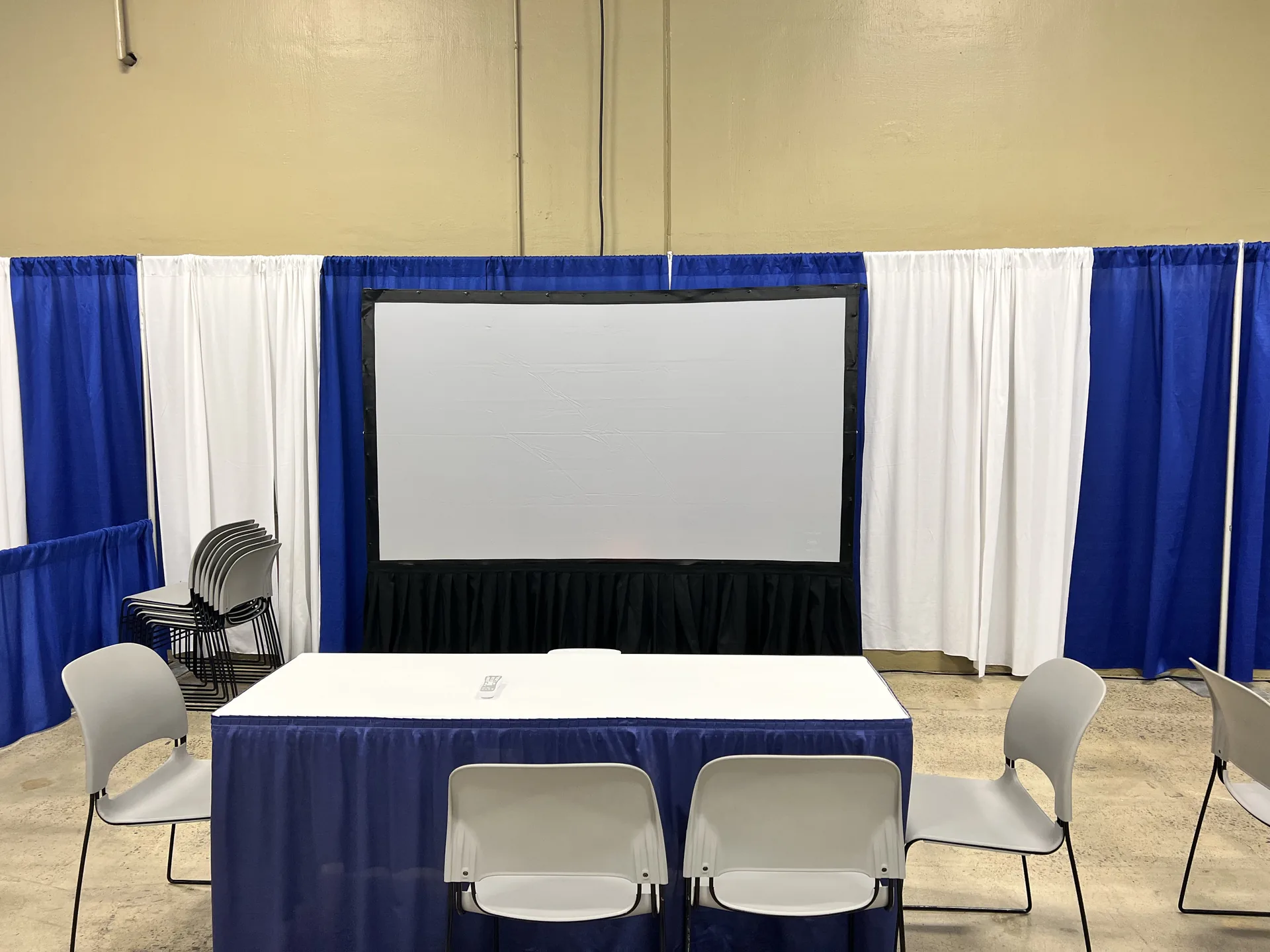 Large projection screen at a conference booth with blue drape