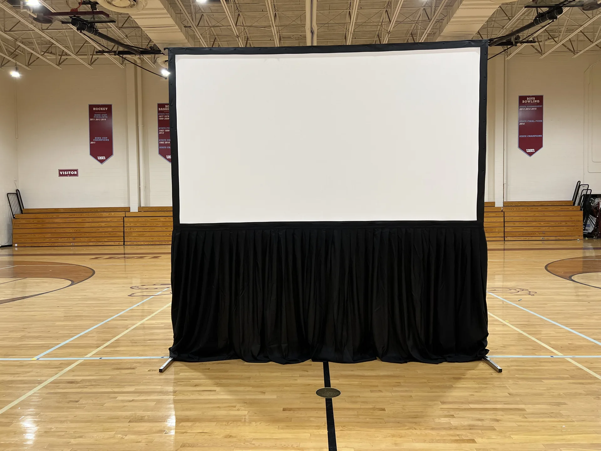 Empty gymnasium with a large projection screen set up for an event