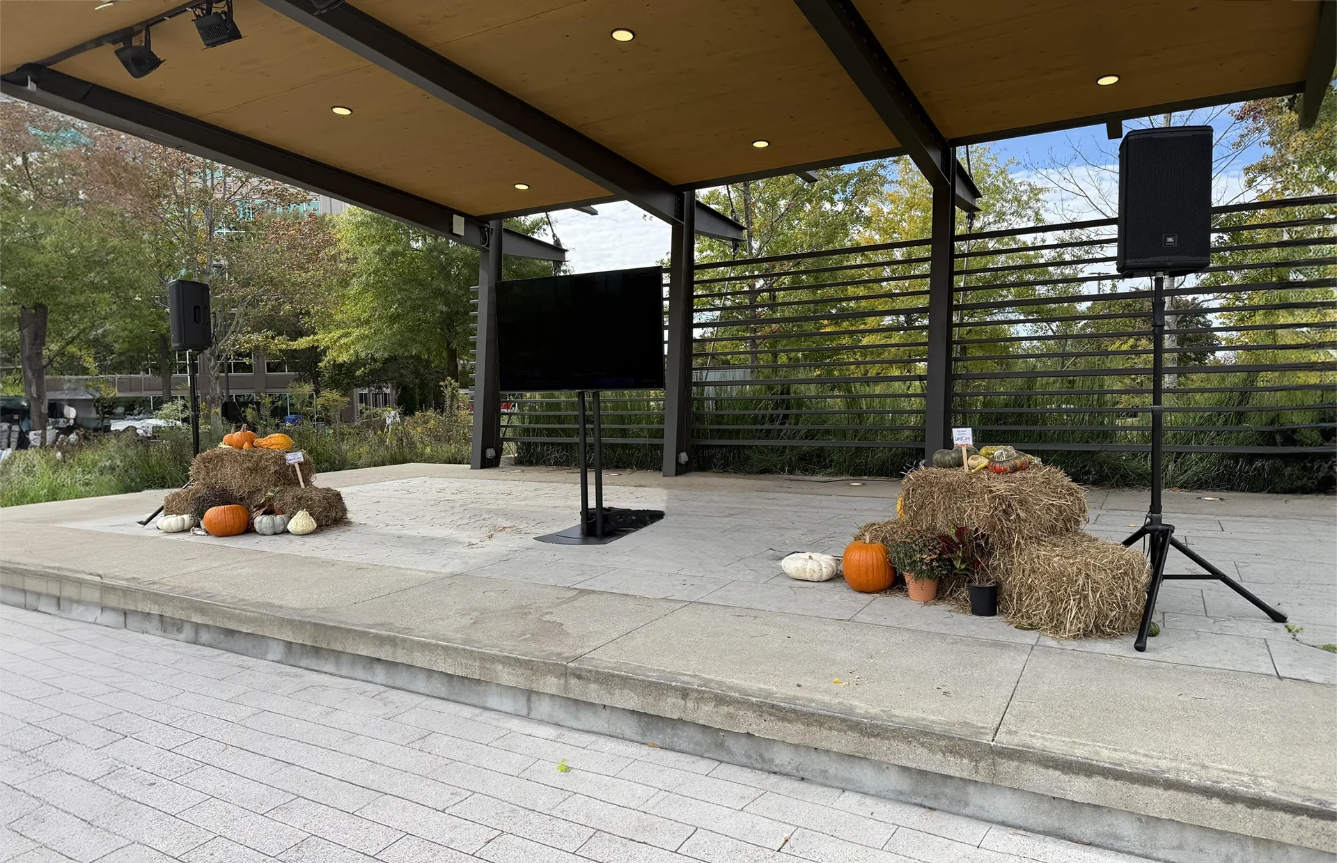 TV display and speaker setup on decorated outdoor stage with hay bales and pumpkins for public event