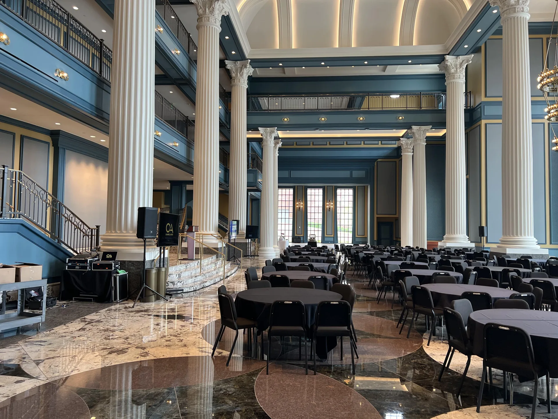 Grand columned hall with two TV displays, PA speakers, stage and banquet seating