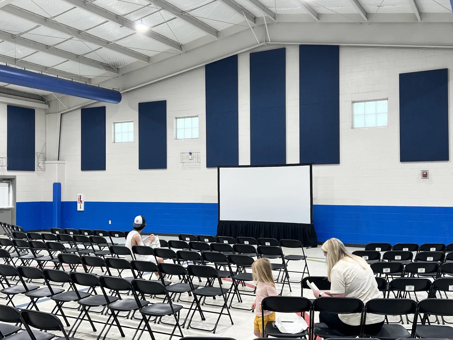 Indoor auditorium setup with black chairs facing a large projection screen