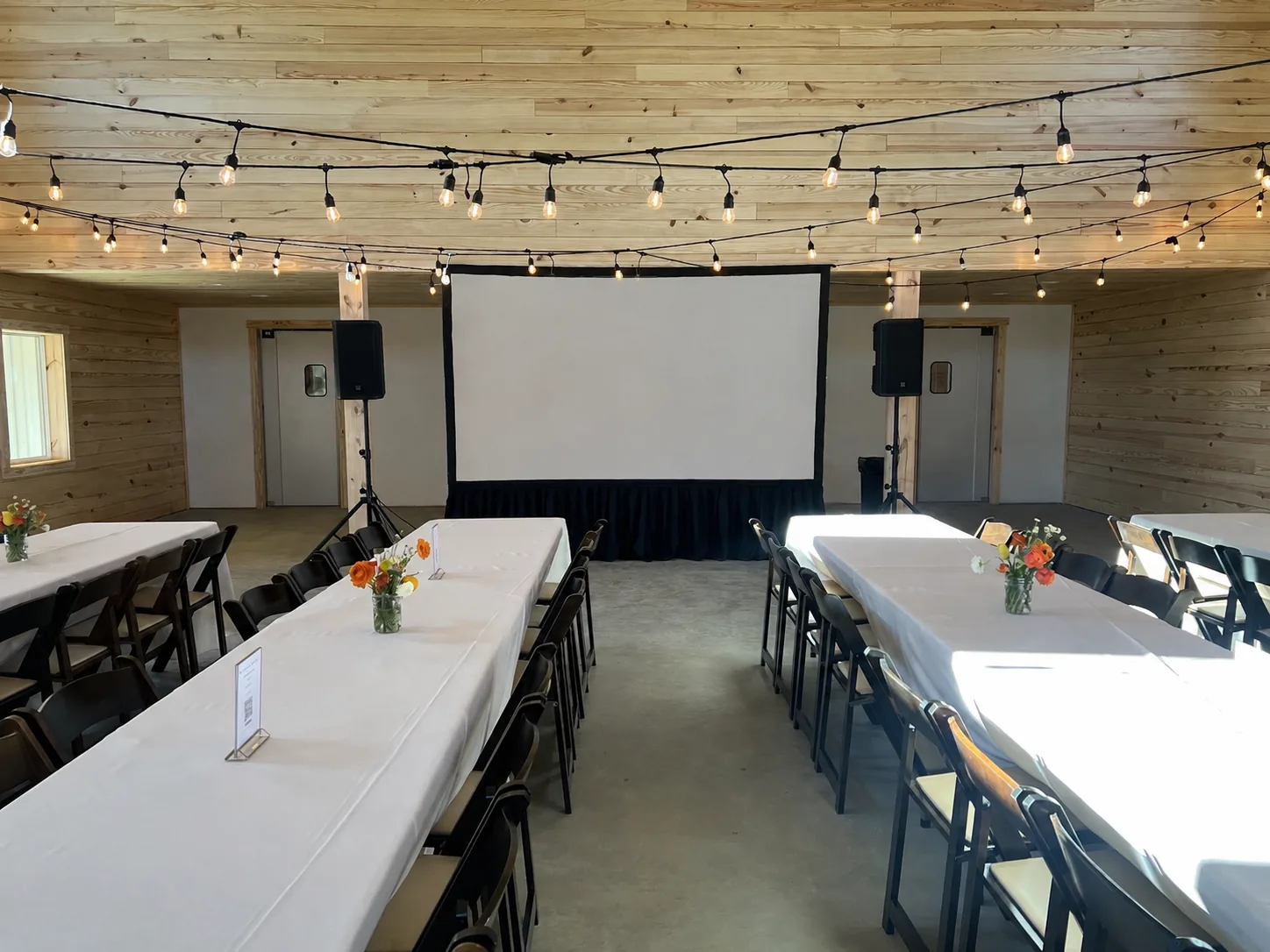 Indoor dining event with projection screen, PA speakers and long banquet tables