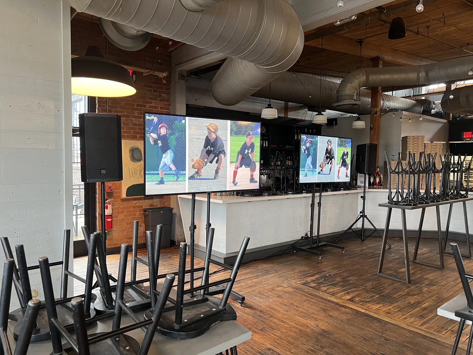 Indoor event setup with three TVs displaying sports highlights and PA speakers in an industrial venue