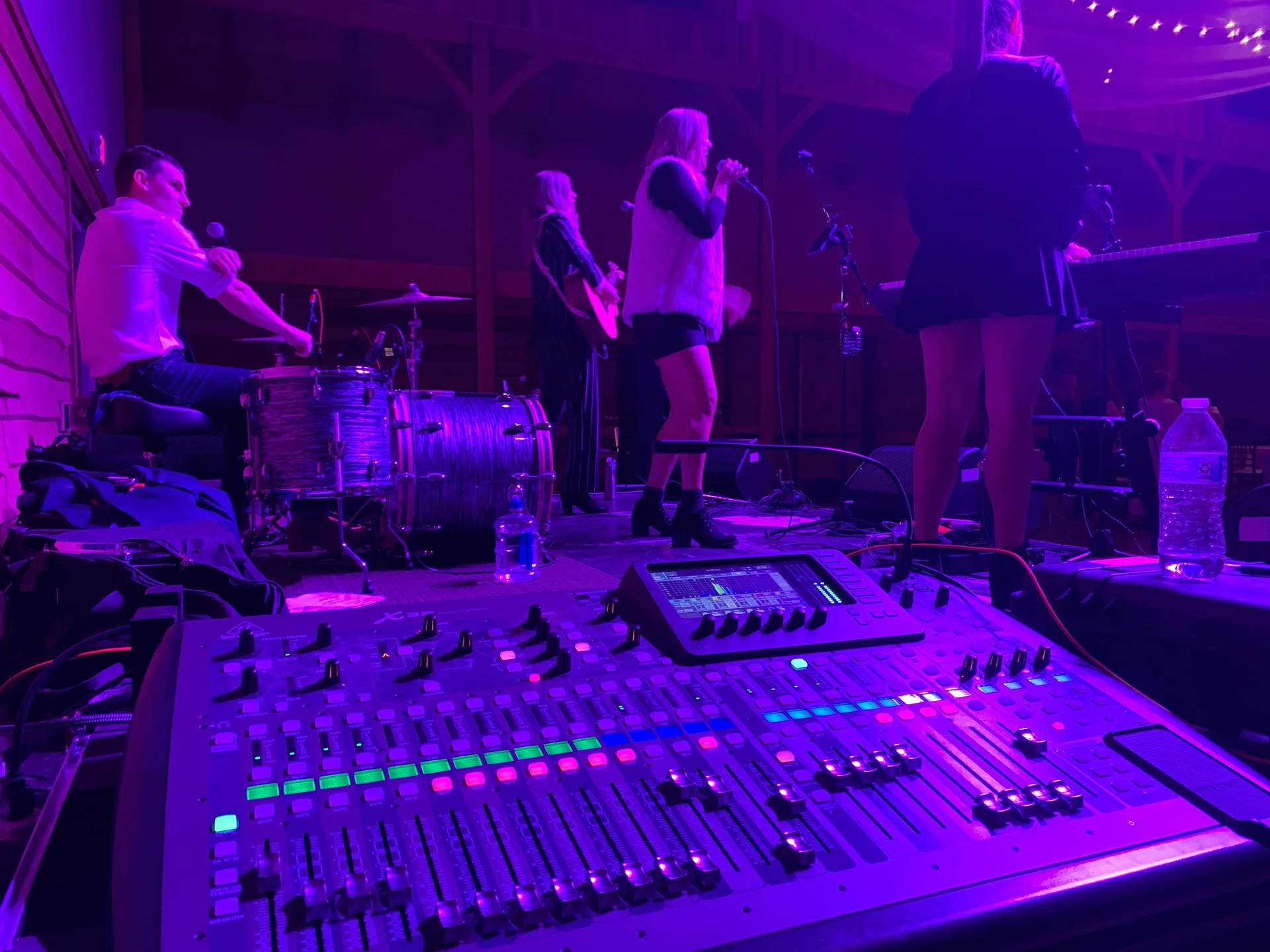 Close-up of a mixing board with a live band performing on stage in the background