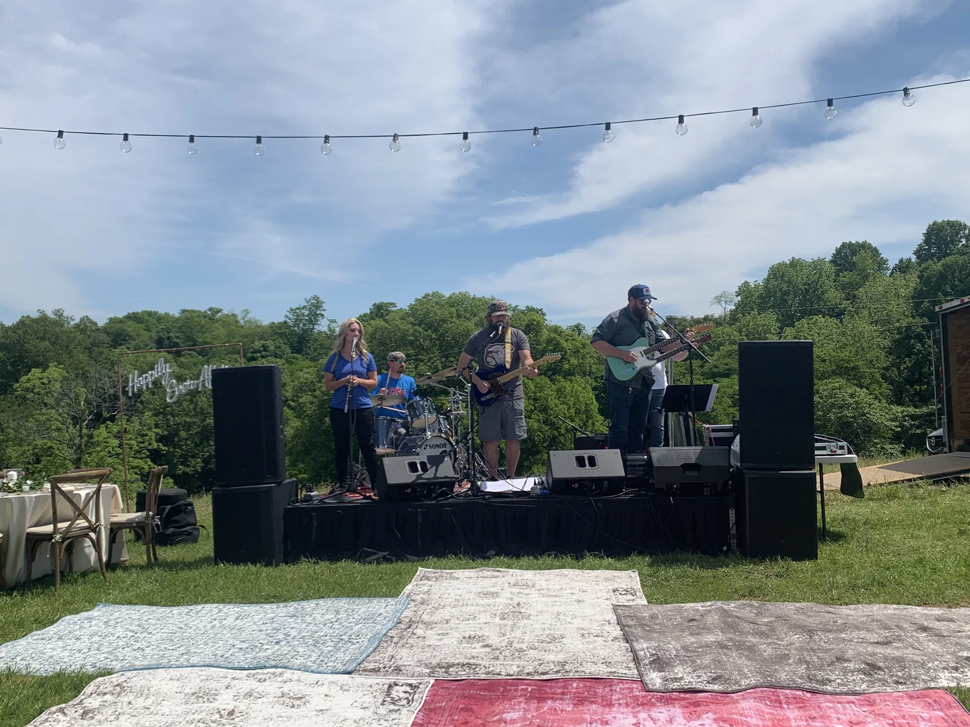Live band performing outdoors on a hillside with string lights and a celebration backdrop