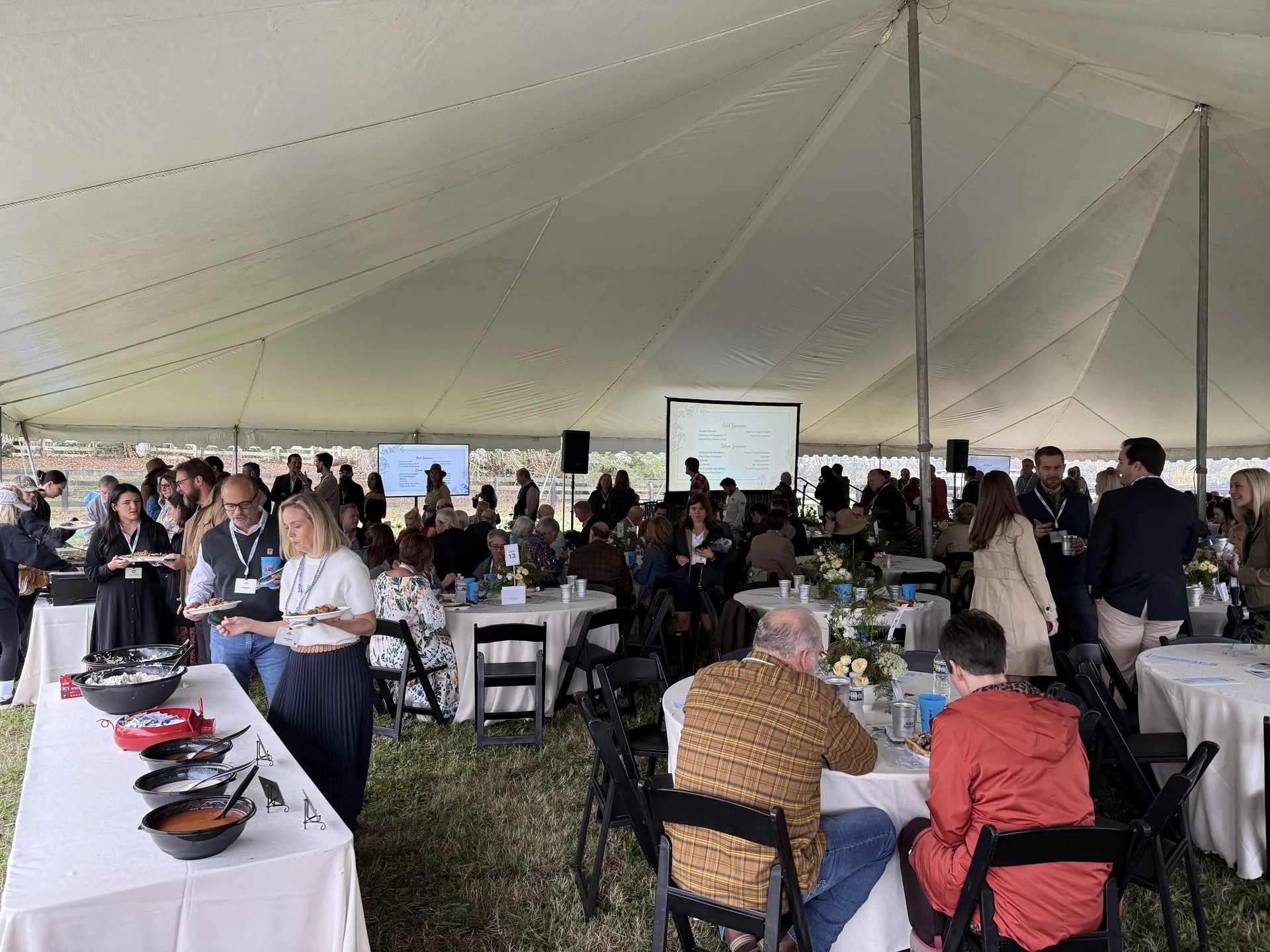 Guests dining under an outdoor tent with projection screens and PA speakers