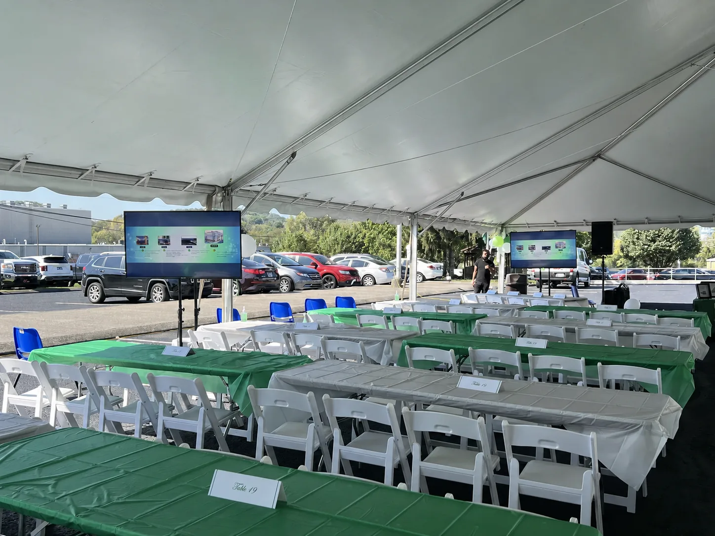 Outdoor event stage setup with a podium, TVs, and seating under a large tent for a corporate presentation