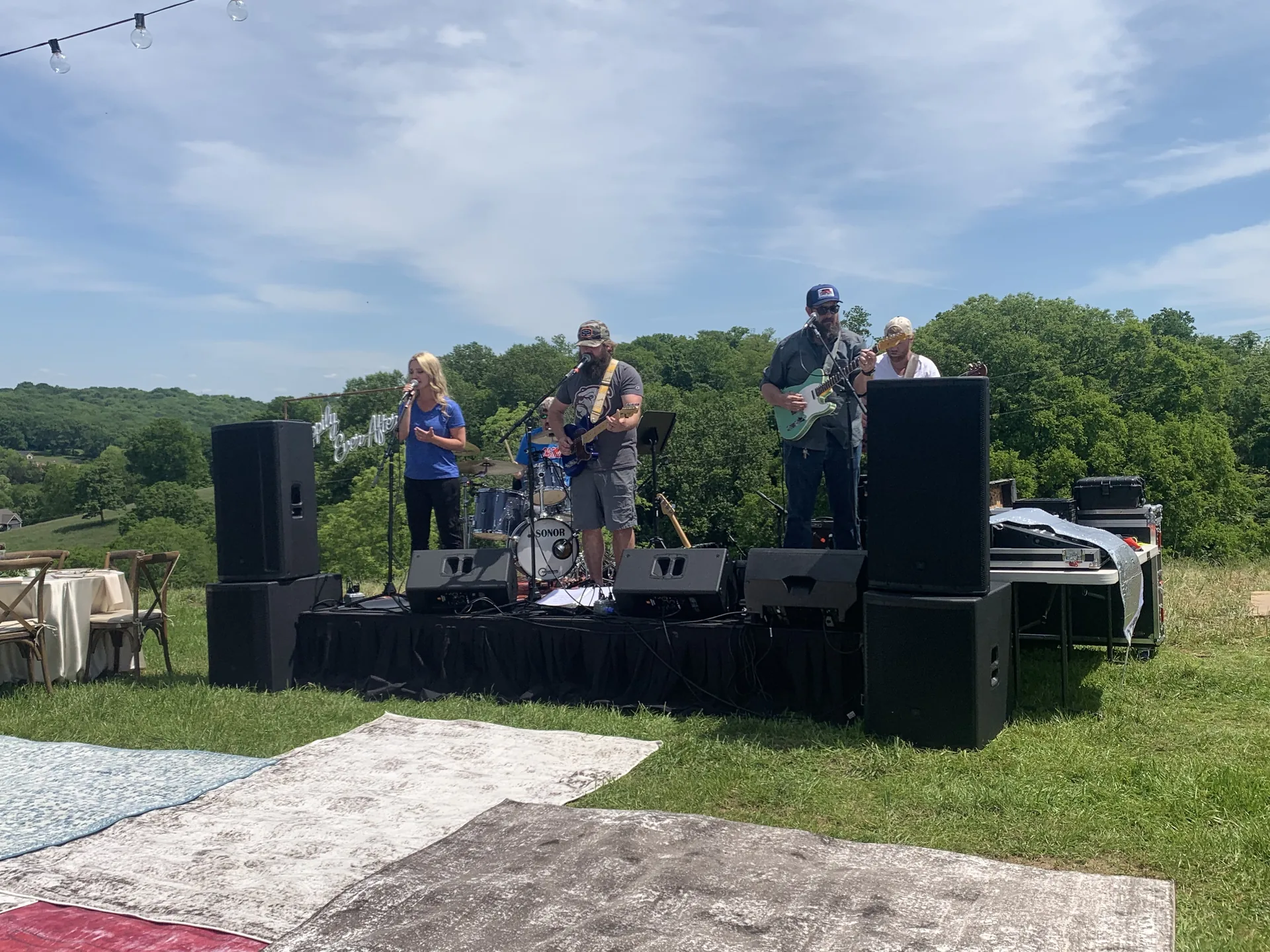 Live band performing outdoors with PA speakers and a scenic backdrop