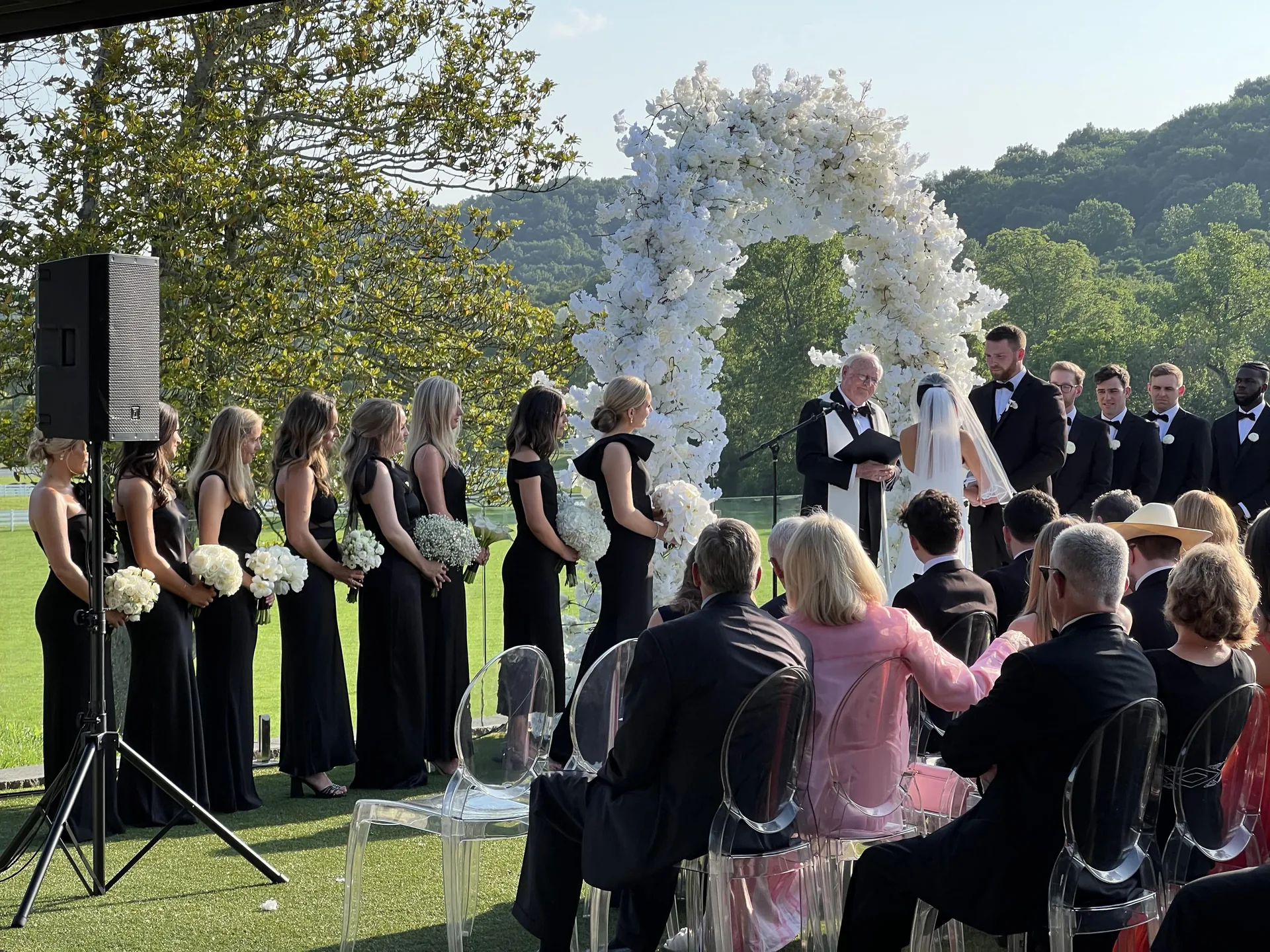 Bride and groom exchanging vows beside a PA speaker at an outdoor wedding ceremony