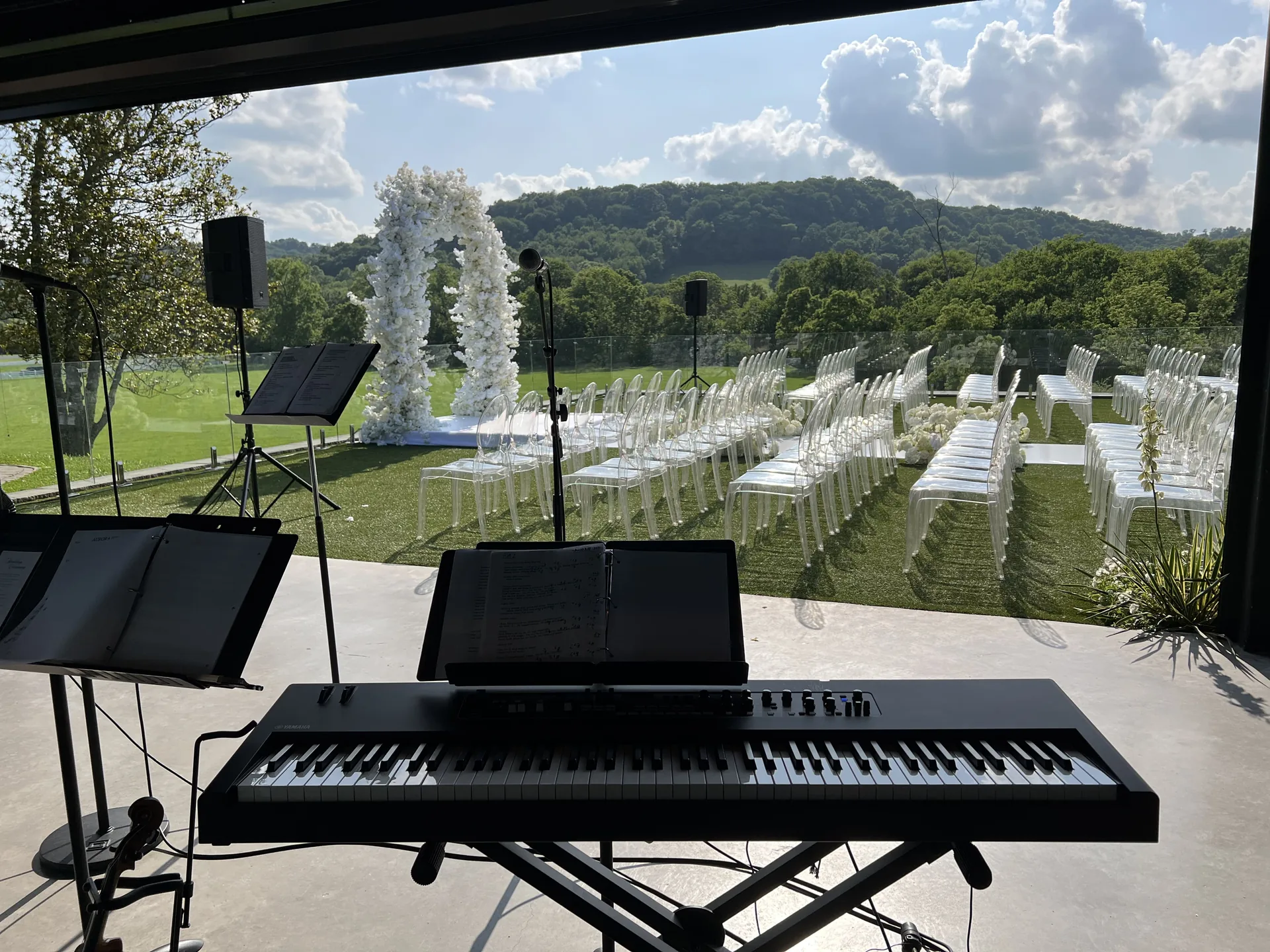 View from behind a keyboard at an outdoor wedding ceremony with chairs and a floral arch in the background