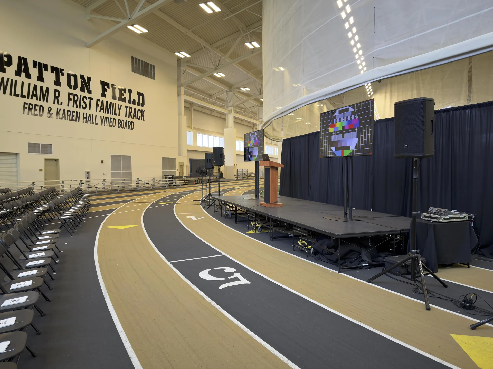 Wide shot of Patton Field indoor track with AV setup for presentation including stage, TVs, and speaker system