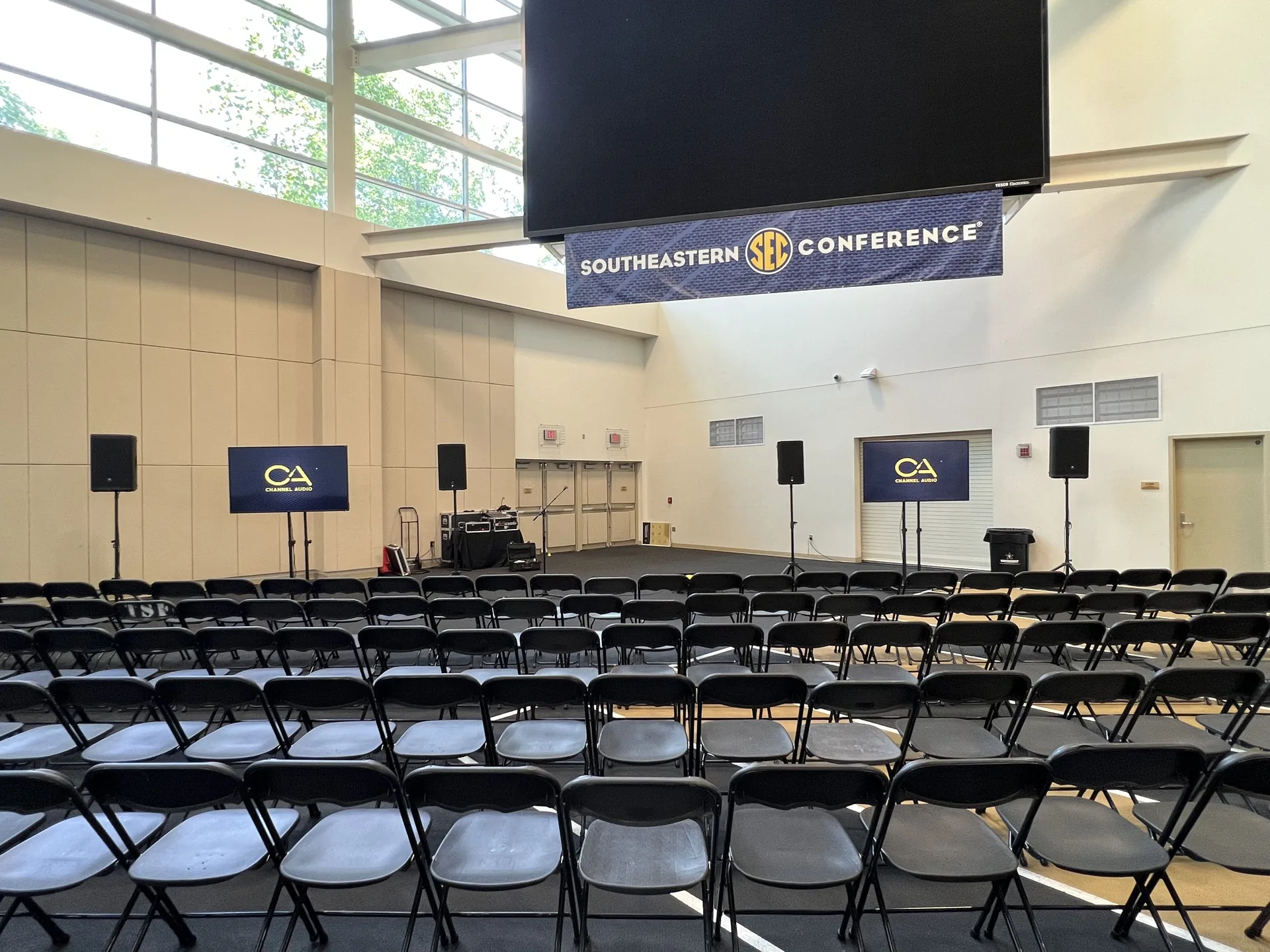 Southeastern Conference presentation setup with a large TV display, four PA speakers and audience seating