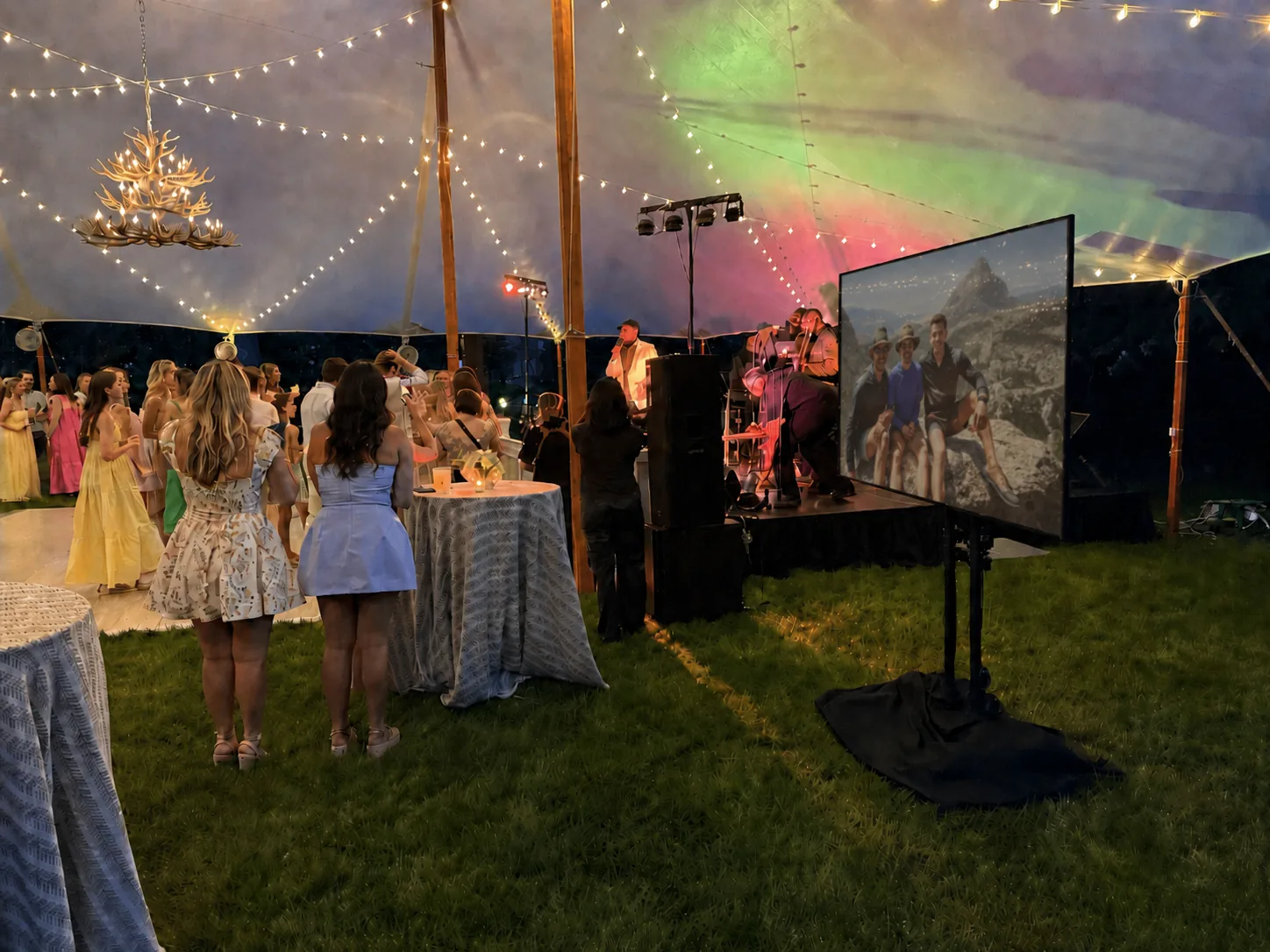 Guests watching a live band at an outdoor event with a large TV display showing visuals