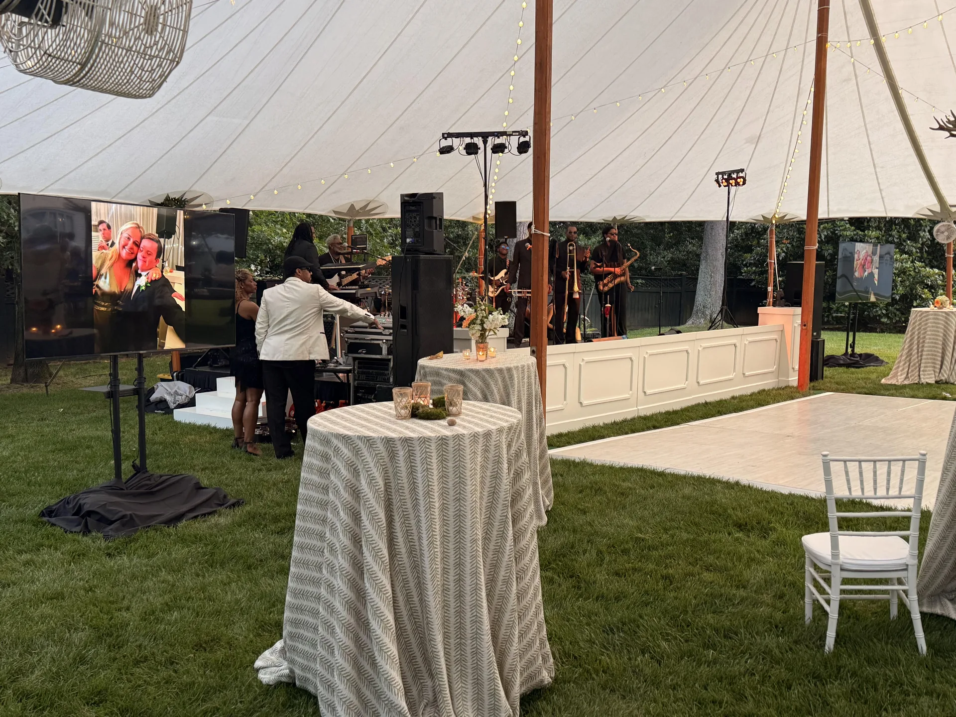 Outdoor tent event with a live band and TV display showing a photo slideshow