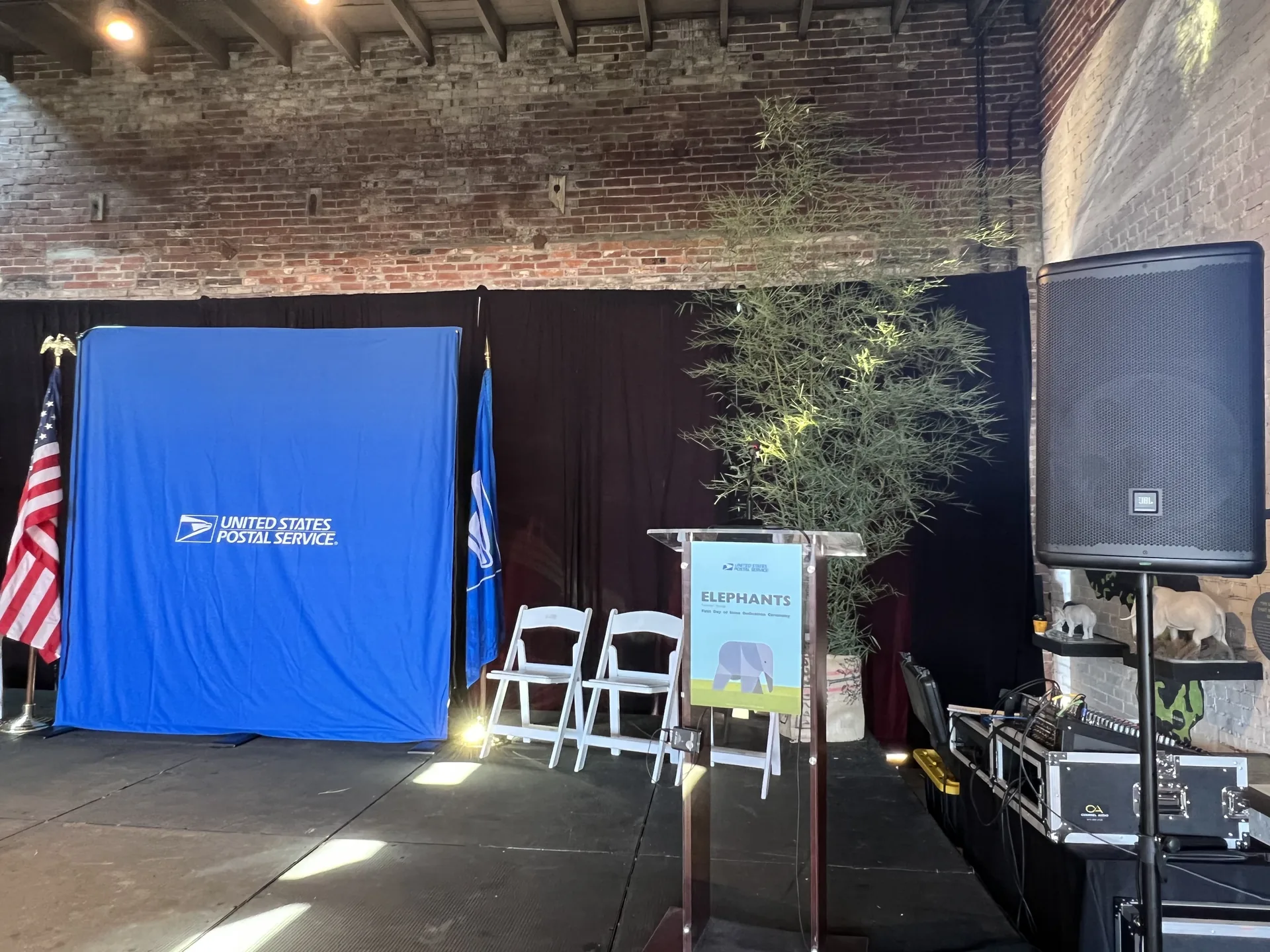 USPS event setup with a branded backdrop, podium and PA audio system in a brick-walled venue
